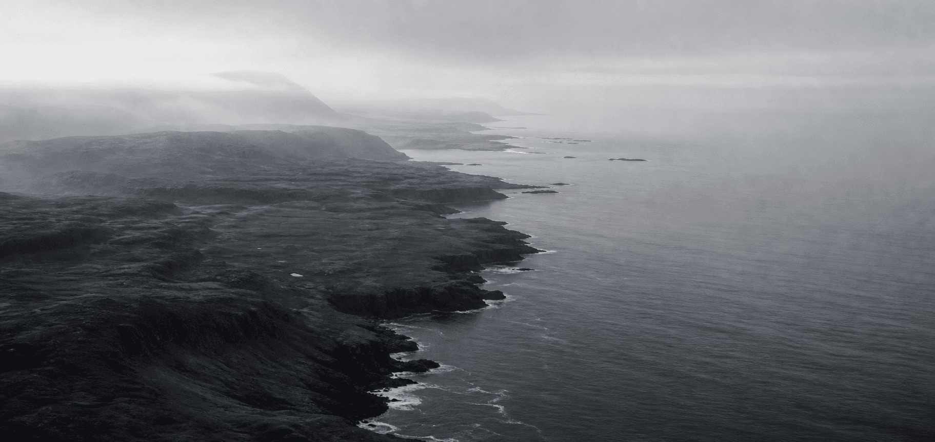 A remote graphite coastline meeting a calm grey ocean